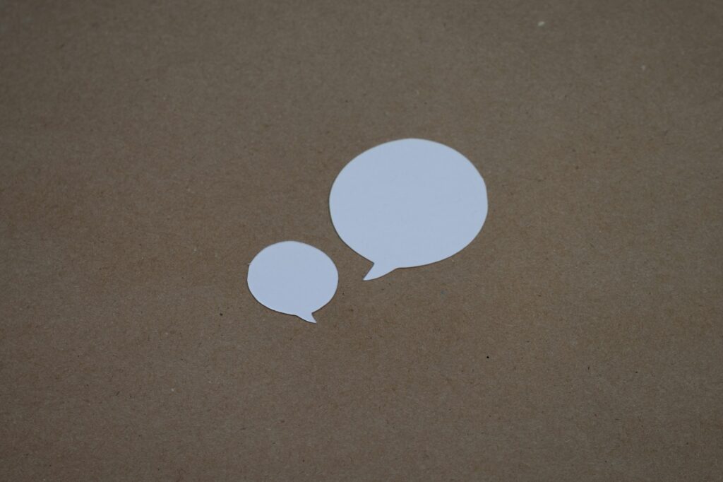 Two white paper speech bubbles on brown cardboard, one small and one large, like a chatbot and a WordPress AI agent